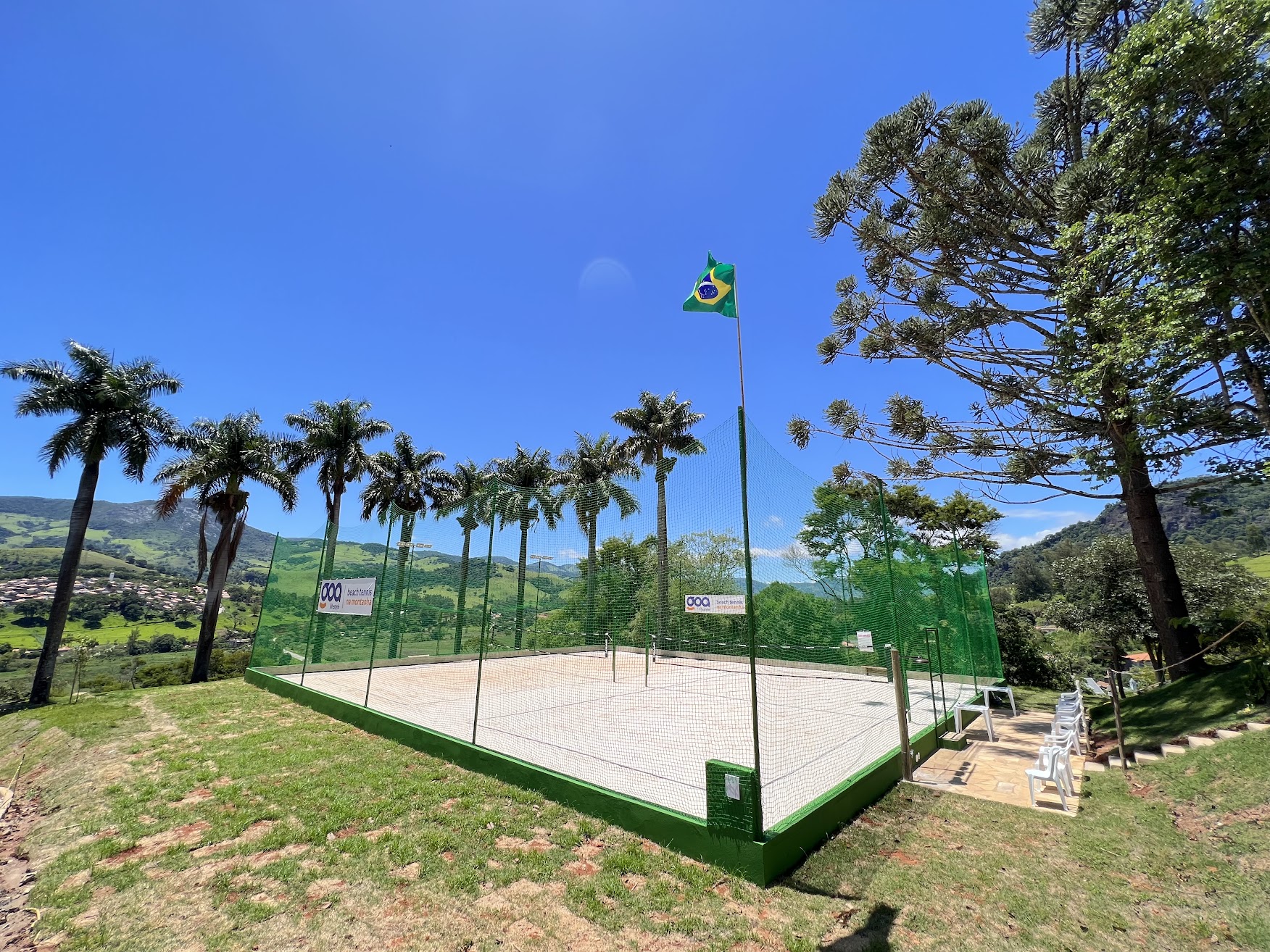 Quadra de areia do GOA rodeada de palmeiras imperiais, com vista para o vale da Mantiqueira