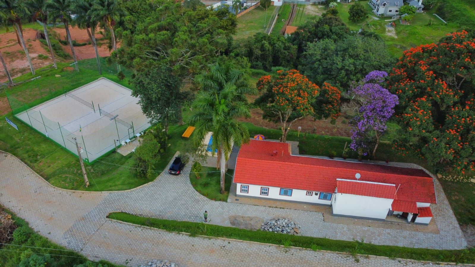 Vista aérea da sede Goa — casa, piscina, quadra de beach tennis e ipês floridos
